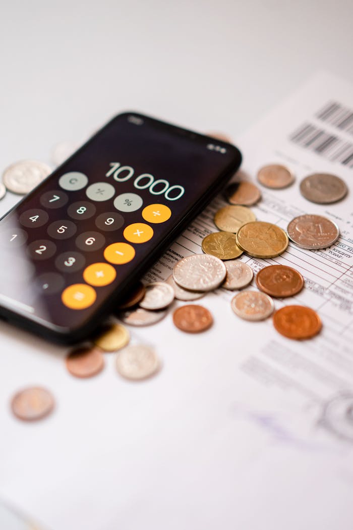 Raising Wealth-Smart Kids: An Advisor’s Blueprint for teaching financial Wisdom Smartphone calculator app displaying 10000 amidst scattered coins and documents.